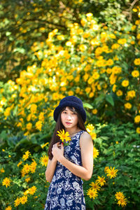 Portrait of a smiling young woman standing on yellow flowering plants