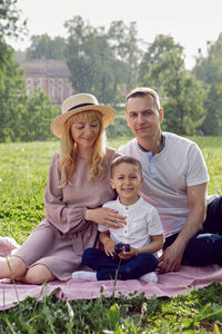 Family with a child a boy of 4 years old. with a car toy sitting on green field under tree in summer 