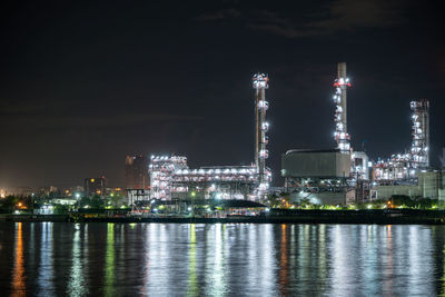 Illuminated city by river against sky at night