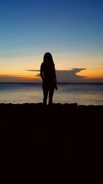 Silhouette woman standing against sea during sunset