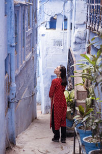 Back view of ethnic female tourist looking up while standing on path near blue buildings on street of jodhpur, india