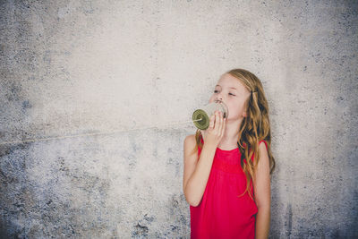 Cute girl playing with tin can phone while standing against wall