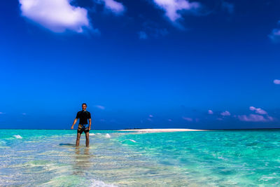 Man standing in sea against blue sky