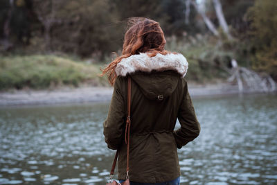 Rear view of woman standing by river during winter