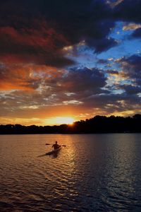 Silhouette man sitting in lake against sky during sunset