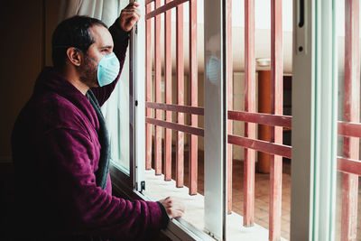 Side view of young man standing against window