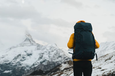 Rear view of man standing on snowcapped mountain against sky