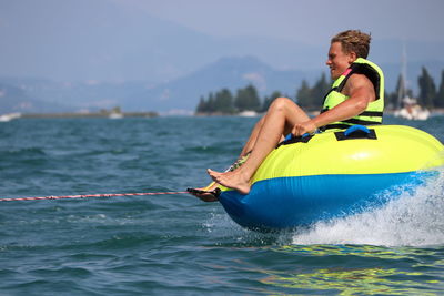 Cheerful teenage boy sitting on inflatable ring in sea