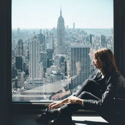 Woman looking at city buildings seen through window