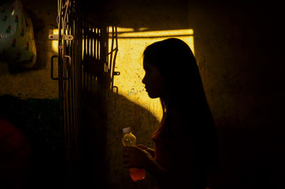 Silhouette woman holding drink in bottle by wall