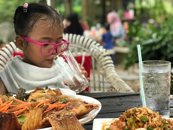 Girl drinking water from glass with food on table