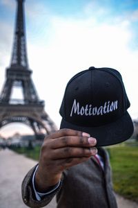 Man holding cap with text while standing against eiffel tower