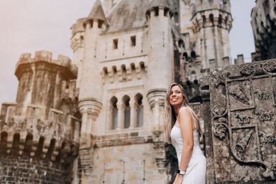 Low angle view of smiling young woman sanding against historical building