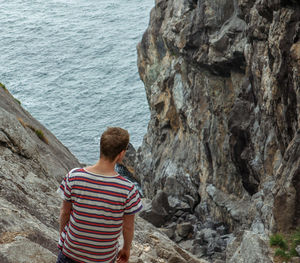 Rear view of woman standing on rock by sea
