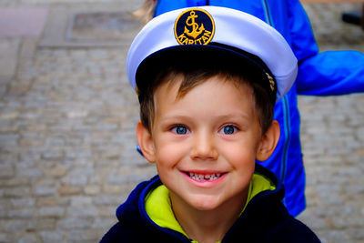 High angle portrait of smiling boy wearing captain cap while standing on street