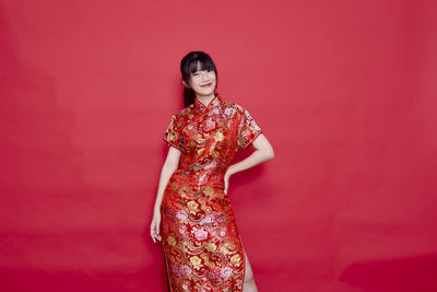 Full length of smiling woman standing against red background