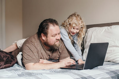 Work from home with kids children. father working on laptop in bedroom with child daughter on back 