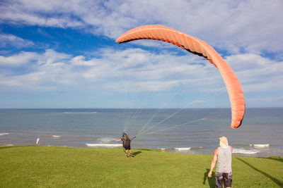 Rear view of people standing on beach against sky