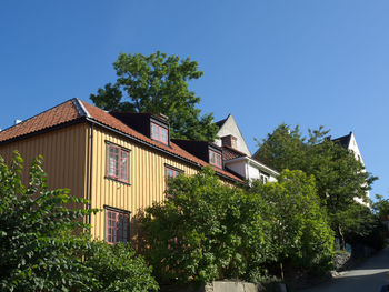 Low angle view of trees and building against clear blue sky