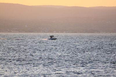 Person on boat in sea against sky during sunset