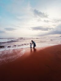 Rear view of woman walking at beach against sky