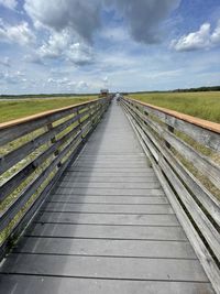 Empty boardwalk leading towards landscape against sky