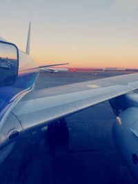 Airplane on runway against sky during sunset