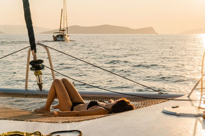 Scenic peaceful view at sunrise of woman on catamaran sailing yacht relaxing at golden hour.