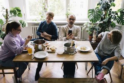 Family using smart phone while sitting on chair at dining table in home