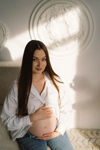 Cute young pregnant girl sitting on the white studio in warm light
