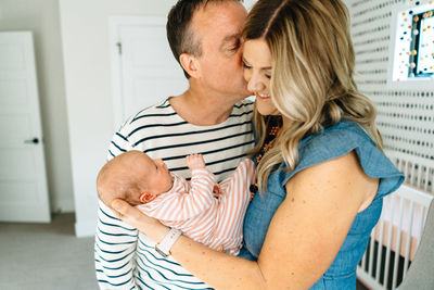 A husband kissing his wife on the cheek while holding a baby