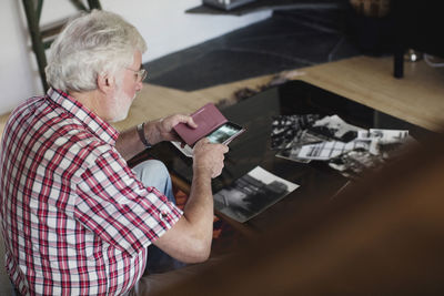 Senior man photographing photographs through smart phone at table