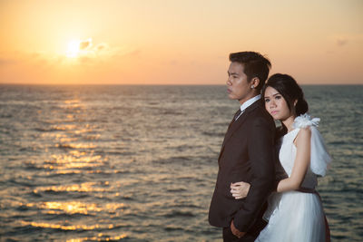 Close-up of couple standing against sea during sunset
