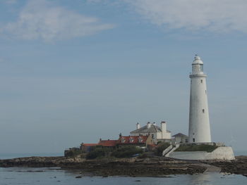 Lighthouse amidst sea and buildings against sky