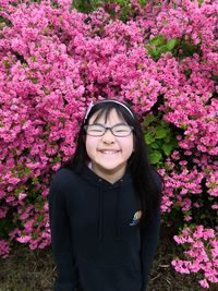Beautiful young woman with pink flower standing against plants