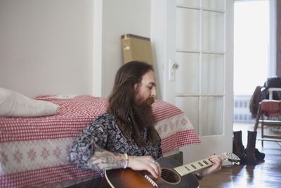Young woman sitting on guitar at home
