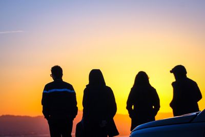 Silhouette of friends standing on landscape at sunset