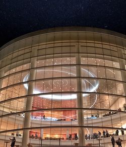 People in illuminated building against clear sky at night