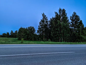 Road amidst trees against clear blue sky