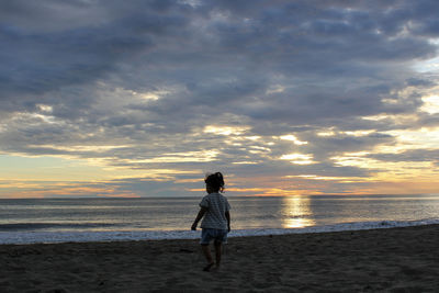 Rear view of man on beach against sky during sunset