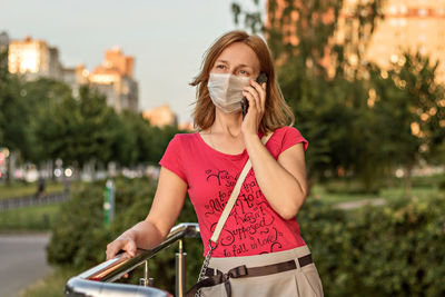 Young woman in a medical protective mask with a smartphone in her hands outdoors. 