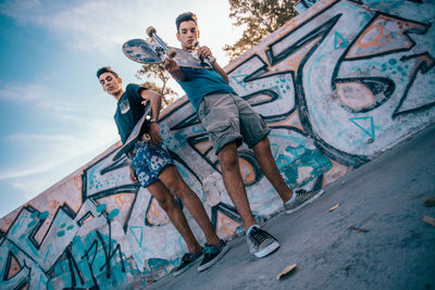 Low angle view of young couple standing against graffiti wall