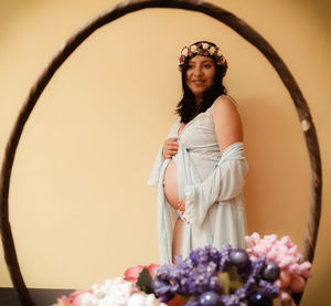 Smiling pregnant woman standing against wall