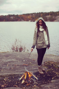 Full length of woman cooking sausage in campfire at lakeshore