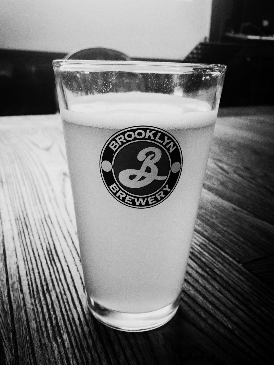 indoors, drink, table, text, refreshment, food and drink, still life, western script, close-up, drinking glass, glass - material, communication, freshness, no people, focus on foreground, single object, white color, wood - material, frothy drink, transparent