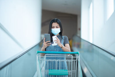 Woman wearing mask holding smart phone on escalator