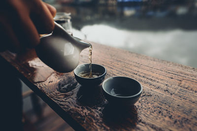 Cropped hand holding tea pot over cup on table