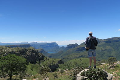 Rear view of man standing on mountain against clear blue sky