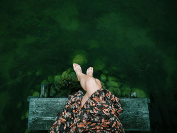 Low section of woman relaxing on pier at lake