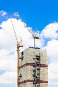 Low angle view of cranes at construction site against sky